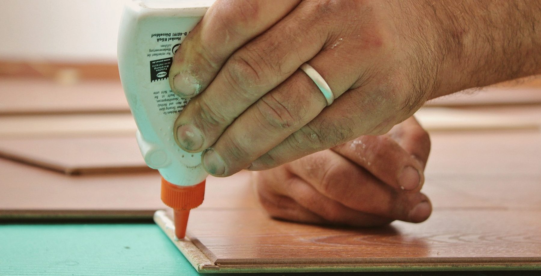 A flooring installer's hands gluing a laminate plank in place